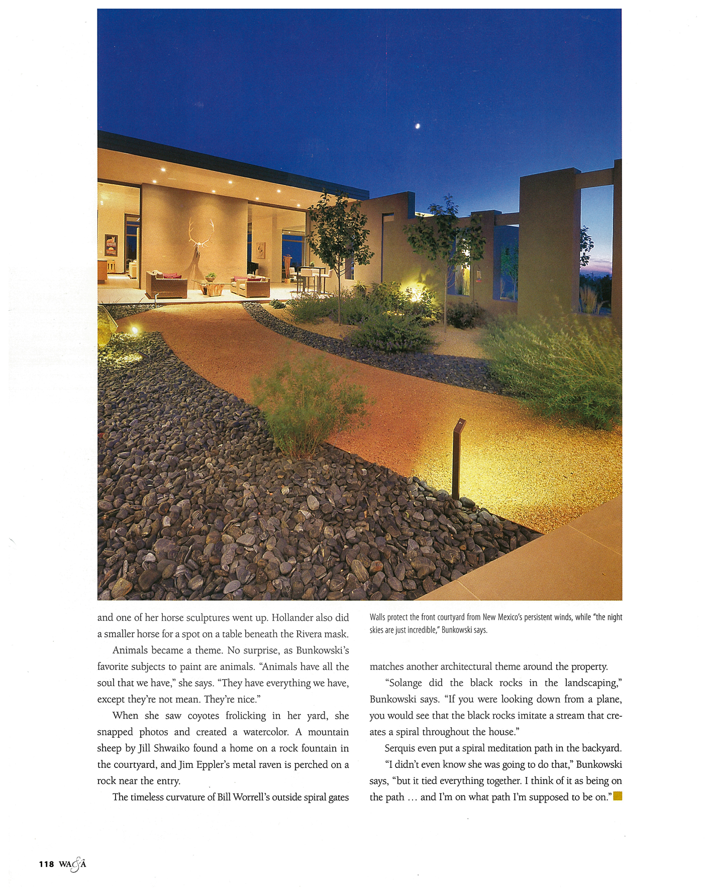 Evening view of a modern Santa Fe home with illuminated landscaping designed by Serquis + Associates, featuring native plants, gravel pathways, and outdoor living spaces.